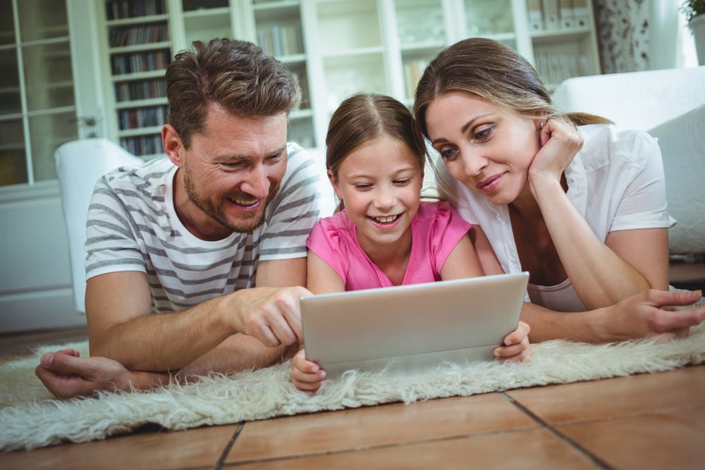 Parents and daughter lying on rug and using digital tablet at home